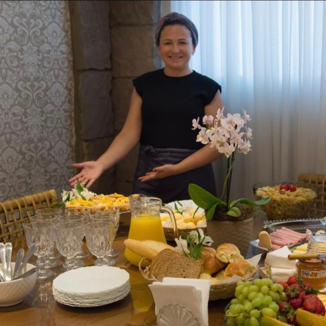 Profissional da Danuta Inbox apresentando uma mesa de coffee-break decorada com frutas, pães, sucos e doces