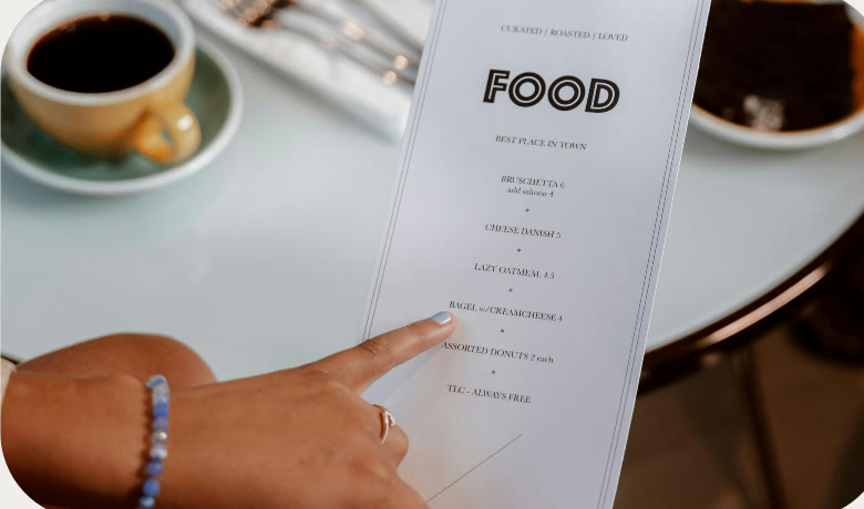 Cliente apontando para um cardápio personalizado sobre a mesa, ao lado de um café